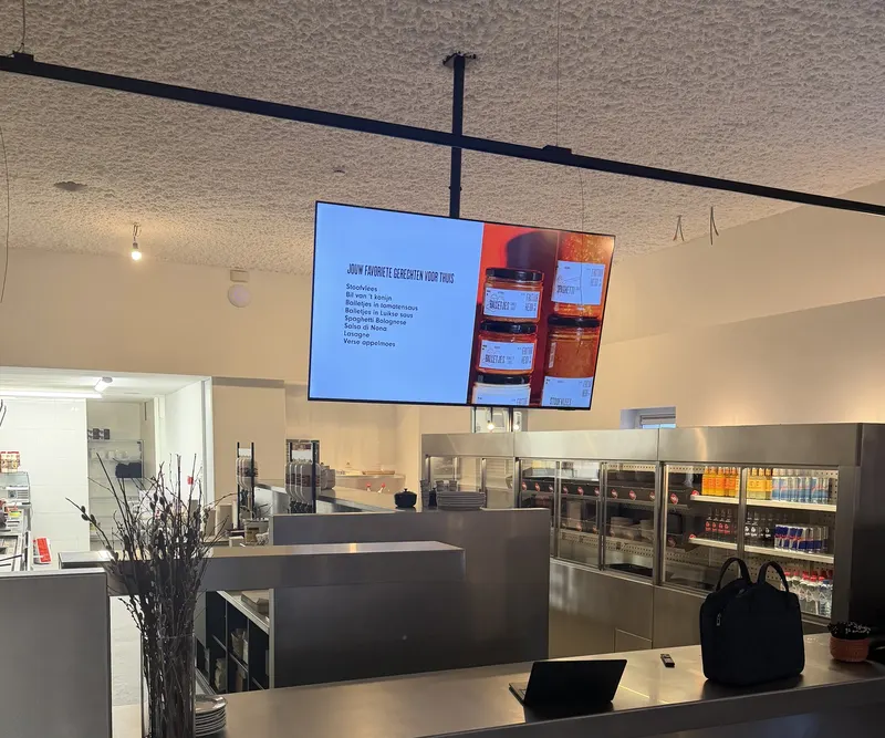 Een hangend digitaal menubord boven de toog bij Frituur Heidi