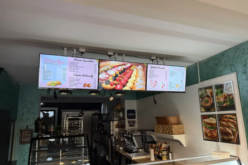 Drie roze digitale menuborden met broodjes, gebak en taarten boven de toog van Irina's bakery